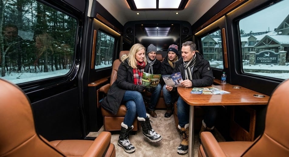 Interior of a black Sprinter shuttle with passengers seated at a table and Deerhurst Resort visible through the window