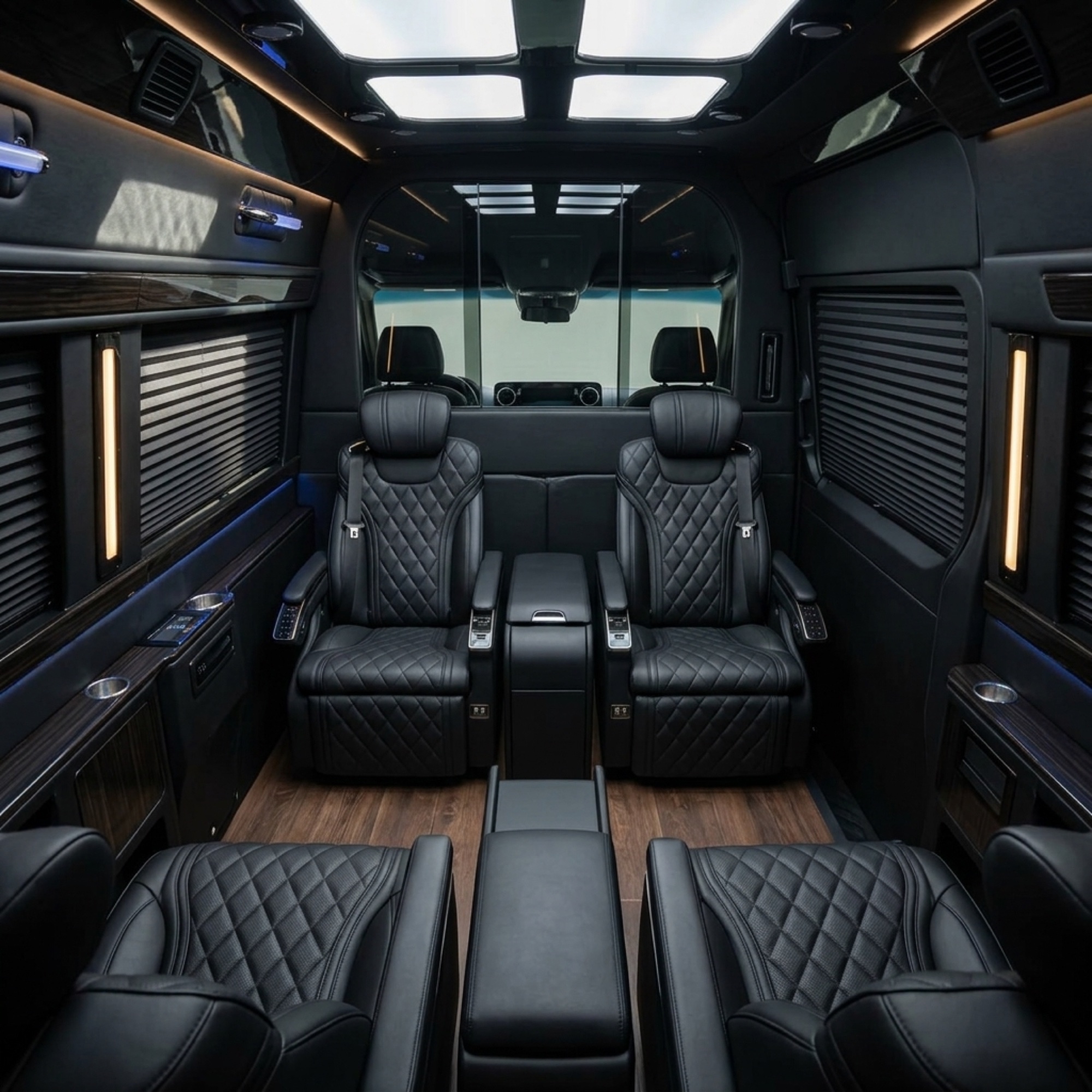 Empty LUX Mercedes Sprinter cabin with four black quilted captain chairs, hardwood floor and ambient lighting