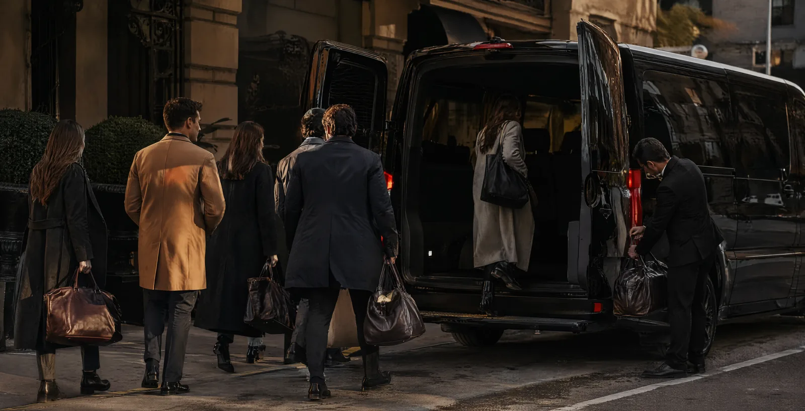 Group of students with overnight bags boarding a black Mercedes Sprinter van