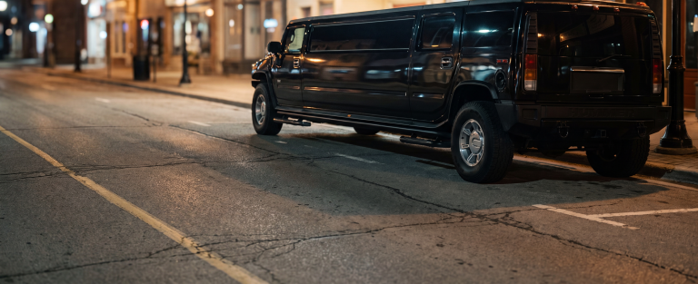 Black Hummer H2 stretch limousine parked at a heritage main street kerb at night