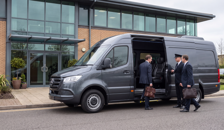 Black Executive Sprinter at a modern office entrance with three businessmen boarding and a uniformed chauffeur at the sliding door