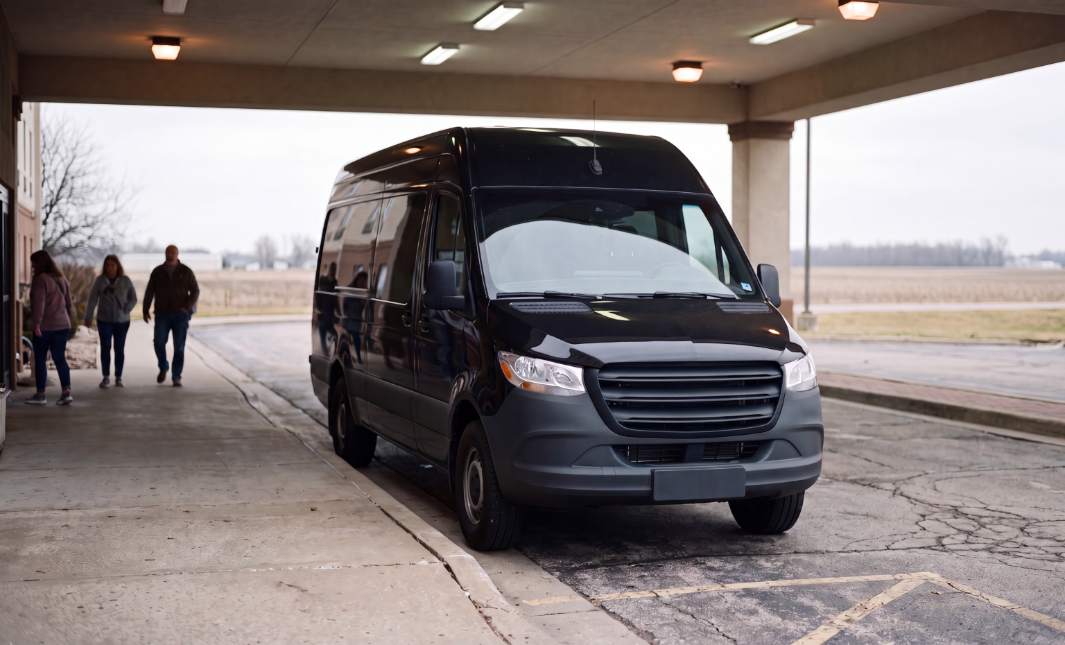 Black Mercedes-Benz Sprinter parked under a covered portico beside a rural Ontario building, with two passengers walking toward it across farmland in the background