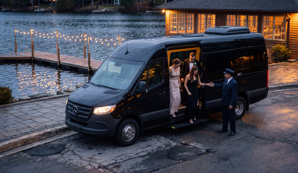 Black Sprinter at a lakeside wedding venue at blue hour, formally dressed guests stepping out under string lights