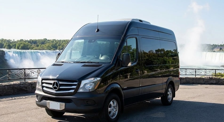 A black Mercedes Sprinter van parked at the Niagara Falls viewing platform with Horseshoe Falls and rising mist visible behind it