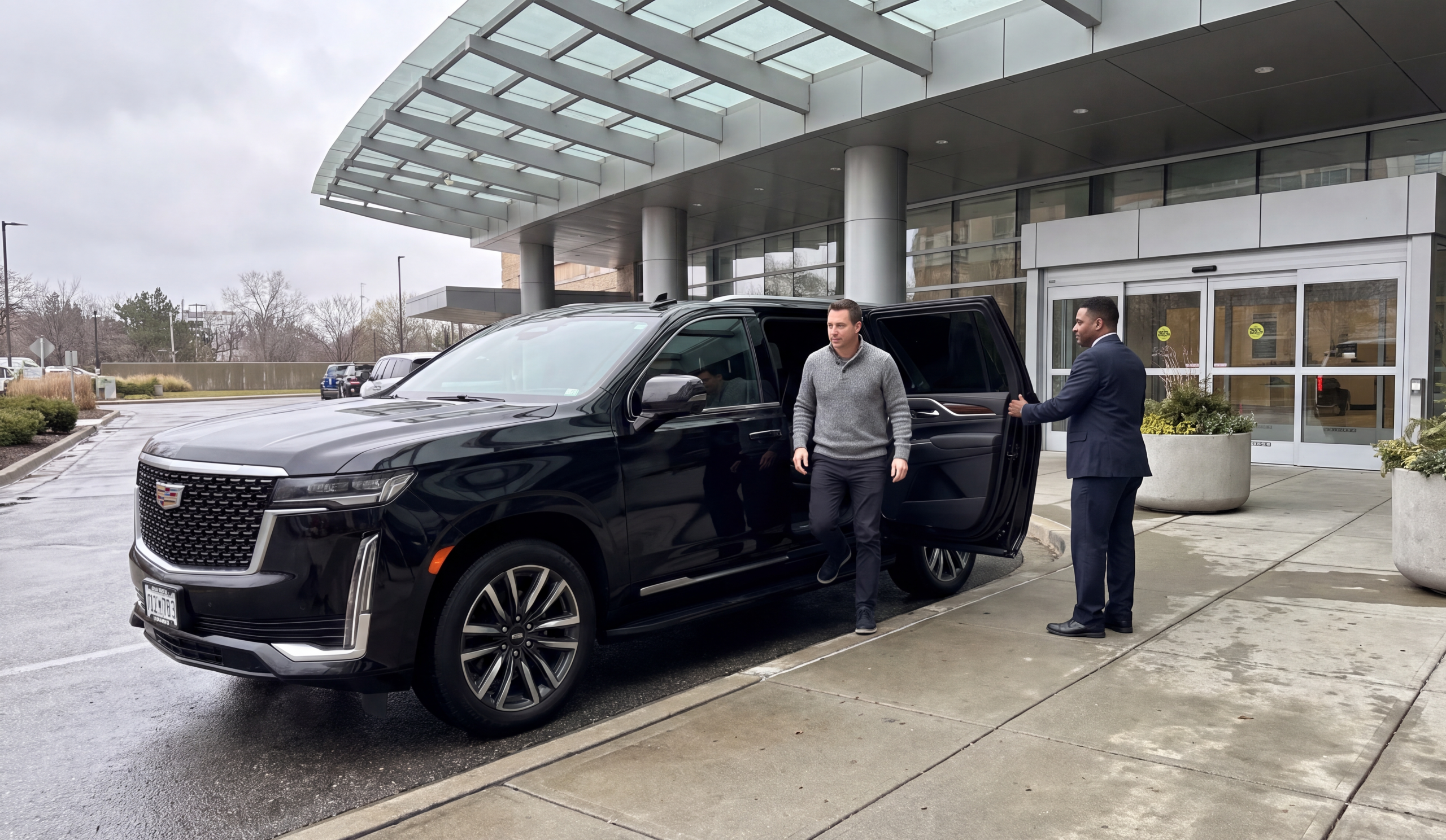 Passenger stepping out of the rear kerb-side door of a black Cadillac Escalade in a hospital entrance loop as the chauffeur holds the door